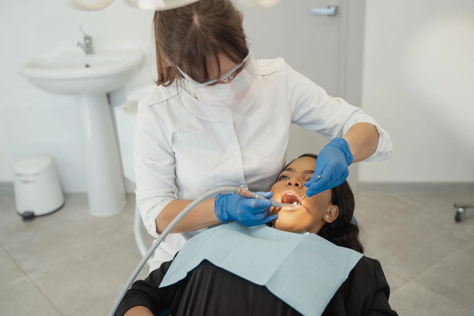 A dentist wearing a facemask examines a patient teeth in a dental clinic.
