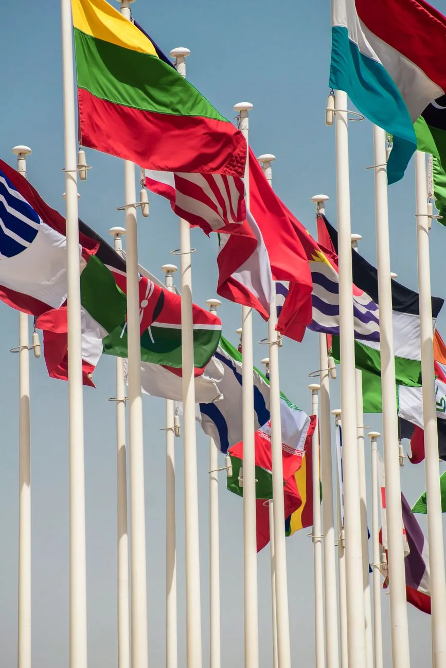 Colorful international flags waving on flagpoles against a clear blue sky.