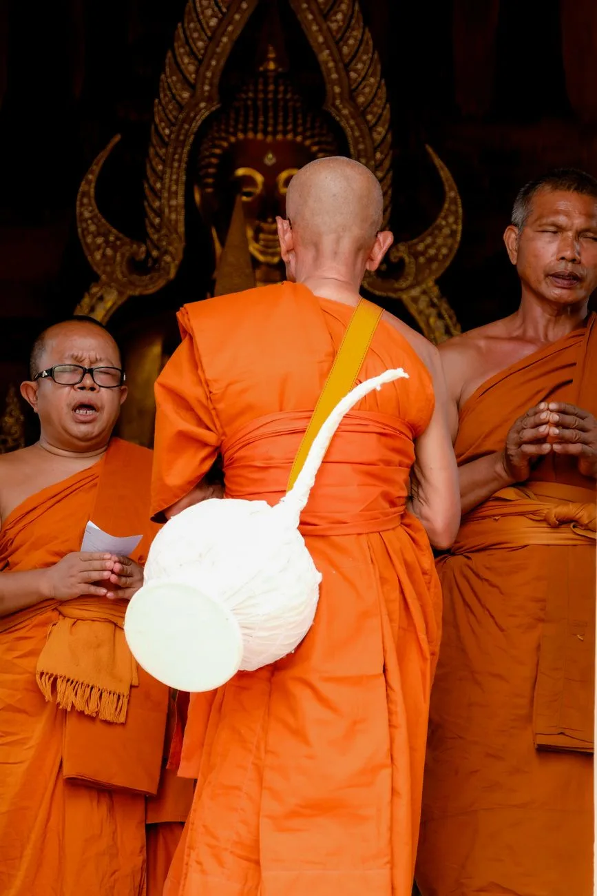 Three Buddhist monks in orange robes standing in prayer at a temple.