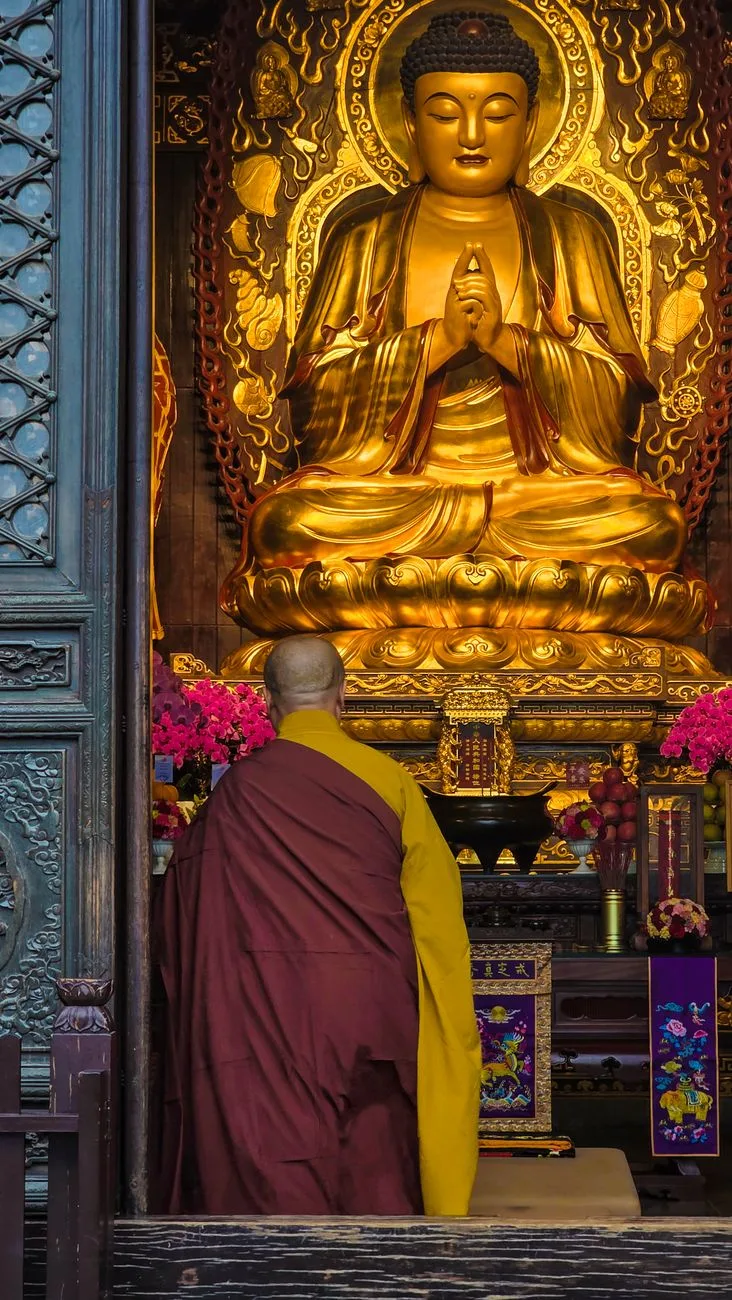 A monk in prayer before a golden Buddha statue.