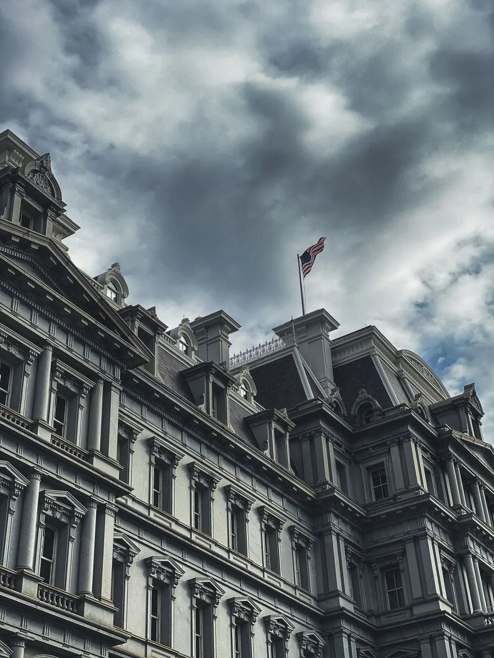 A historic government building with an American flag under dark clouds.