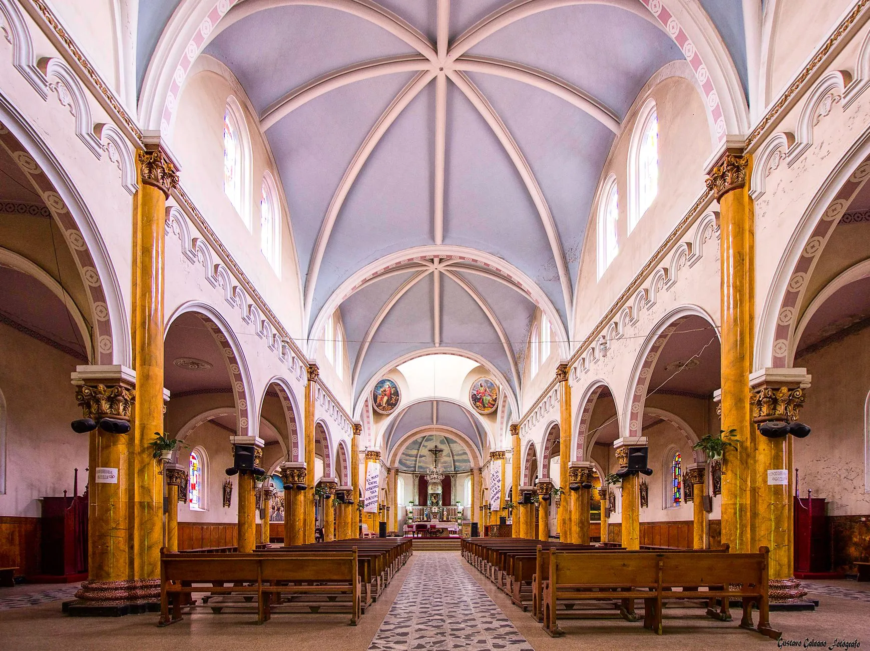 The elegant gold and white interior of a Catholic church with vaulted ceilings.