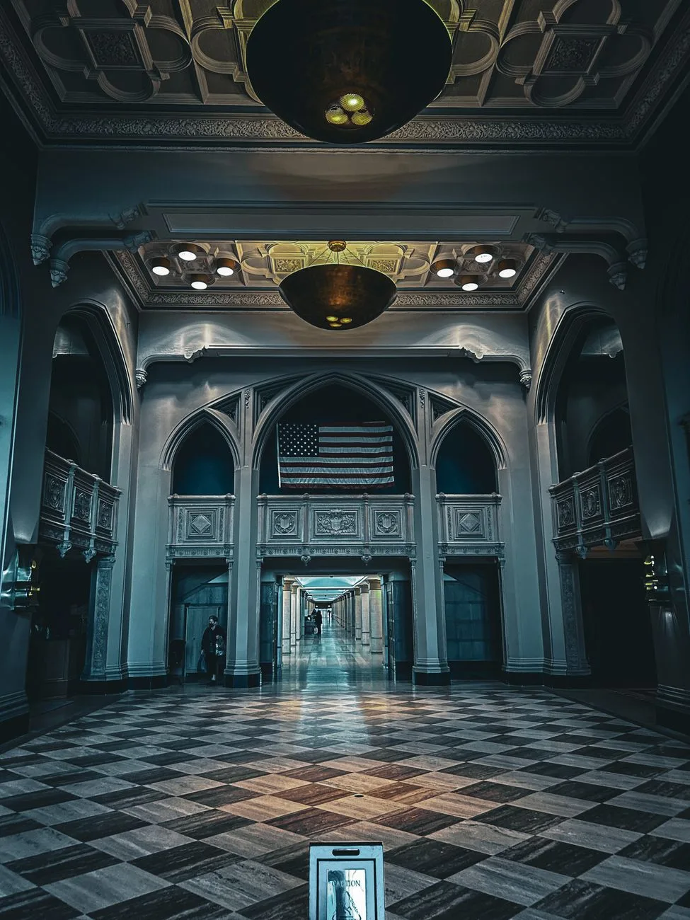 An elegant neoclassical government hallway with chandeliers and a flag.