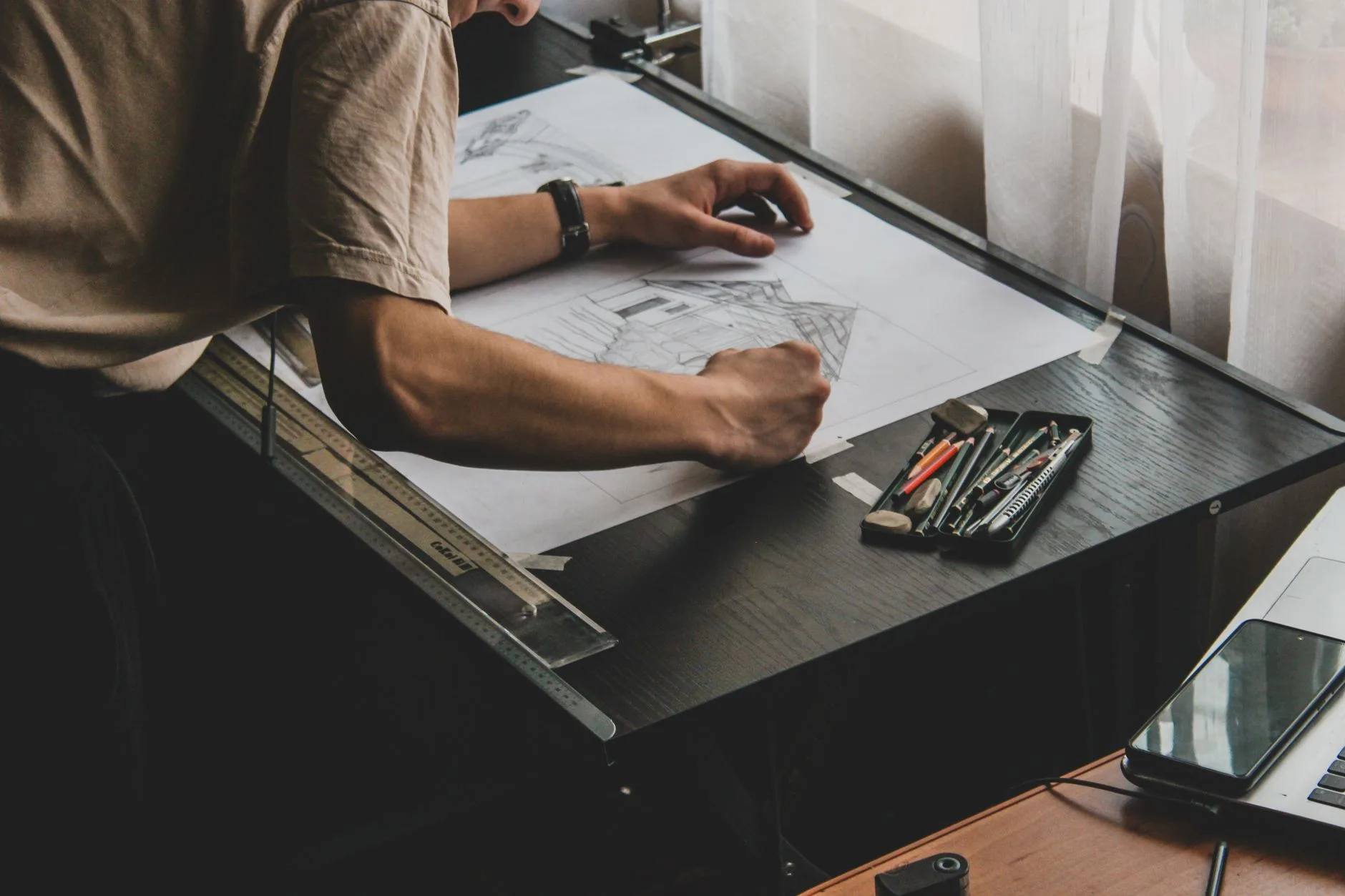 An architect drafting designs on a desk with drawing tools.