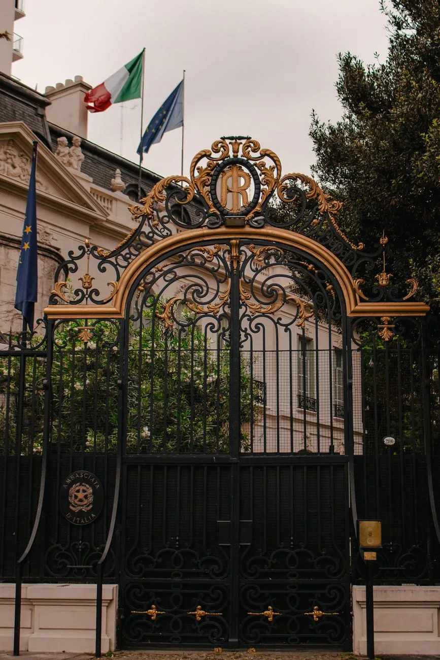 A decorative wrought iron embassy gate with flags.