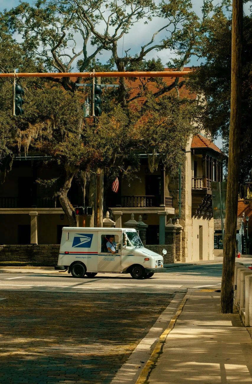 A USPS truck driving through a historic district with cobblestone streets.