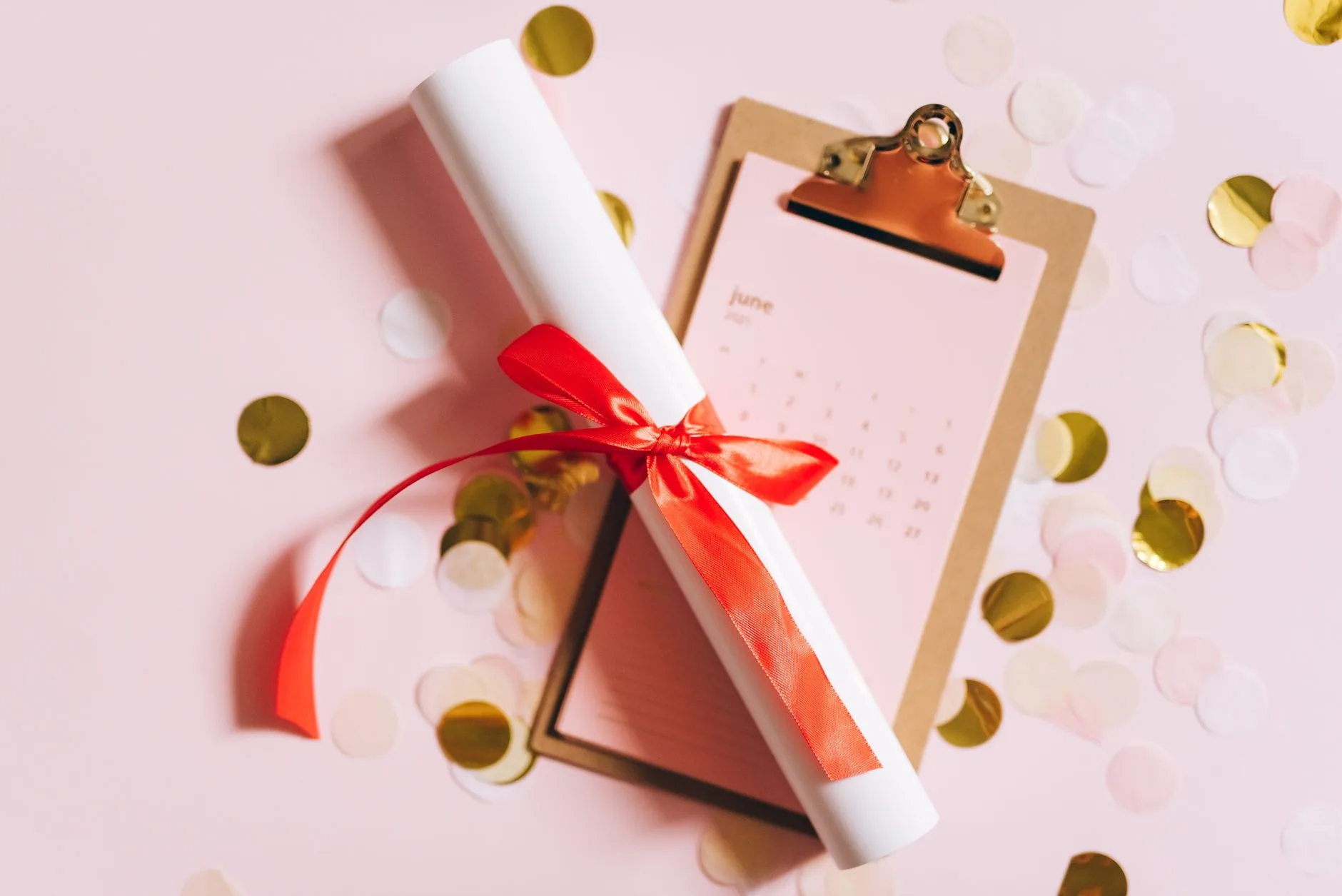 A flat lay of a graduation diploma with a red ribbon and confetti.