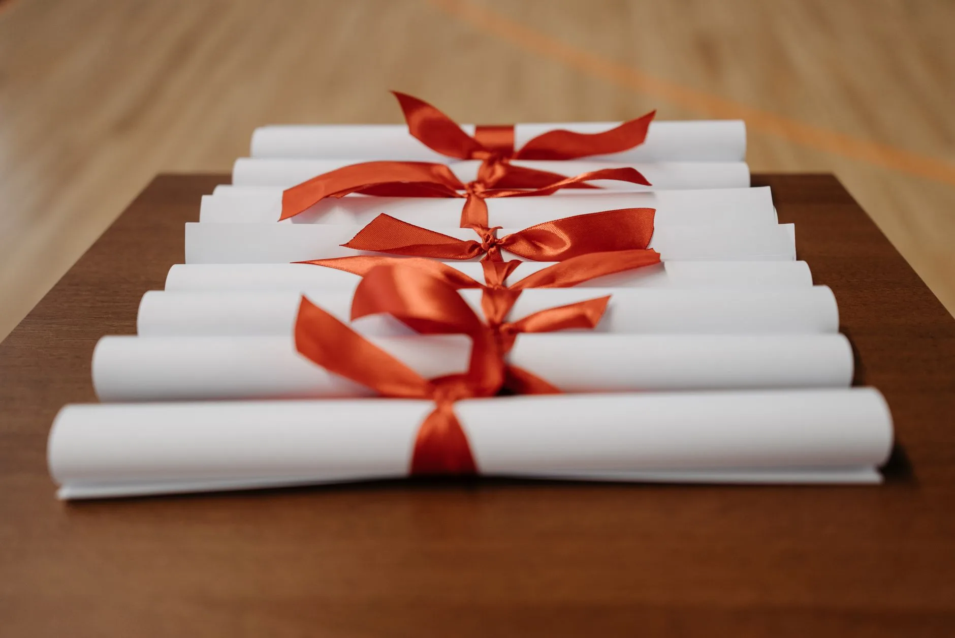 Rolled diplomas tied with red ribbons on a wooden desk.