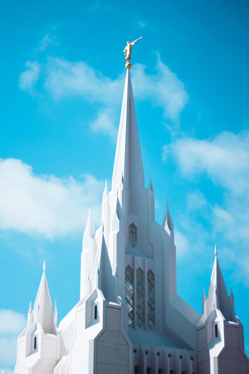 A white LDS temple spire viewed from below against a bright sky.