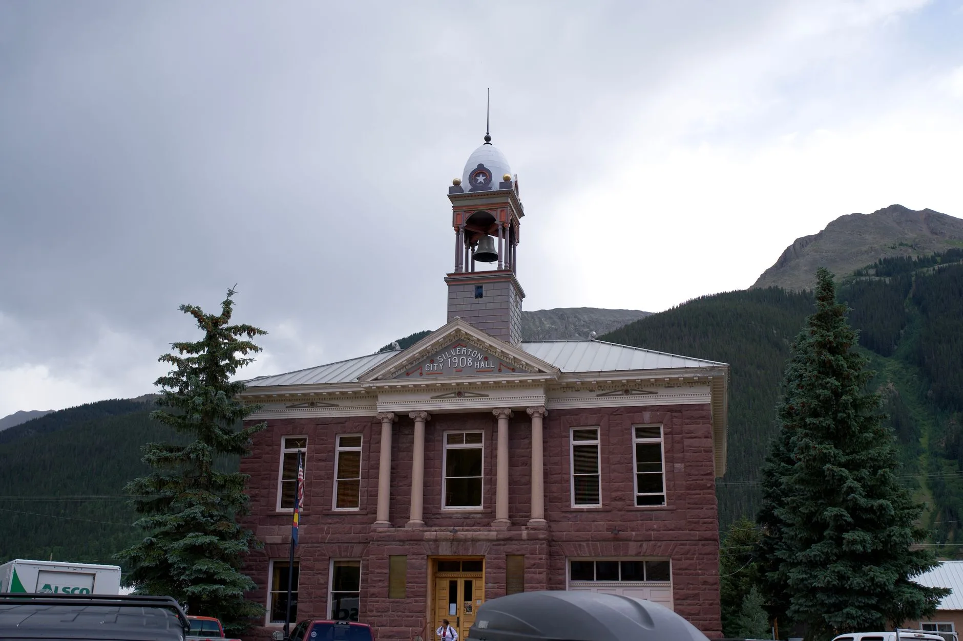A small city hall building set against a mountain backdrop.