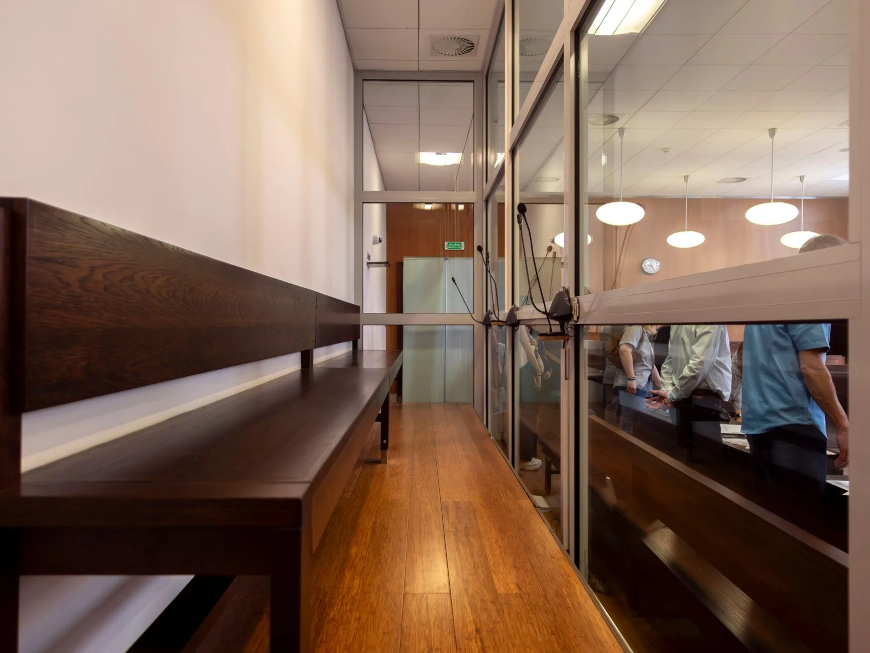 A courtroom interior with wooden benches and a glass partition.