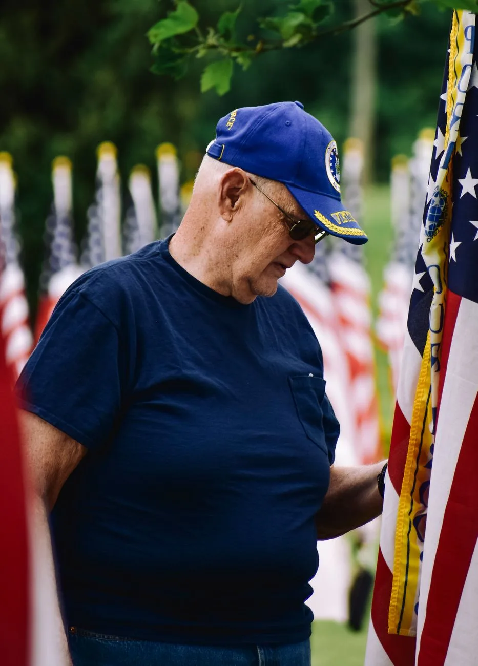 A senior veteran standing beside American flags.