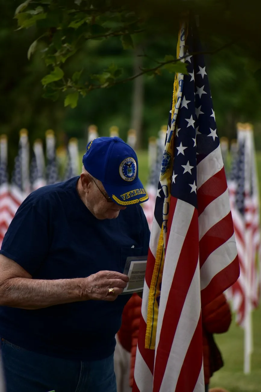 A senior veteran in a contemplative moment beside an American flag ceremony.