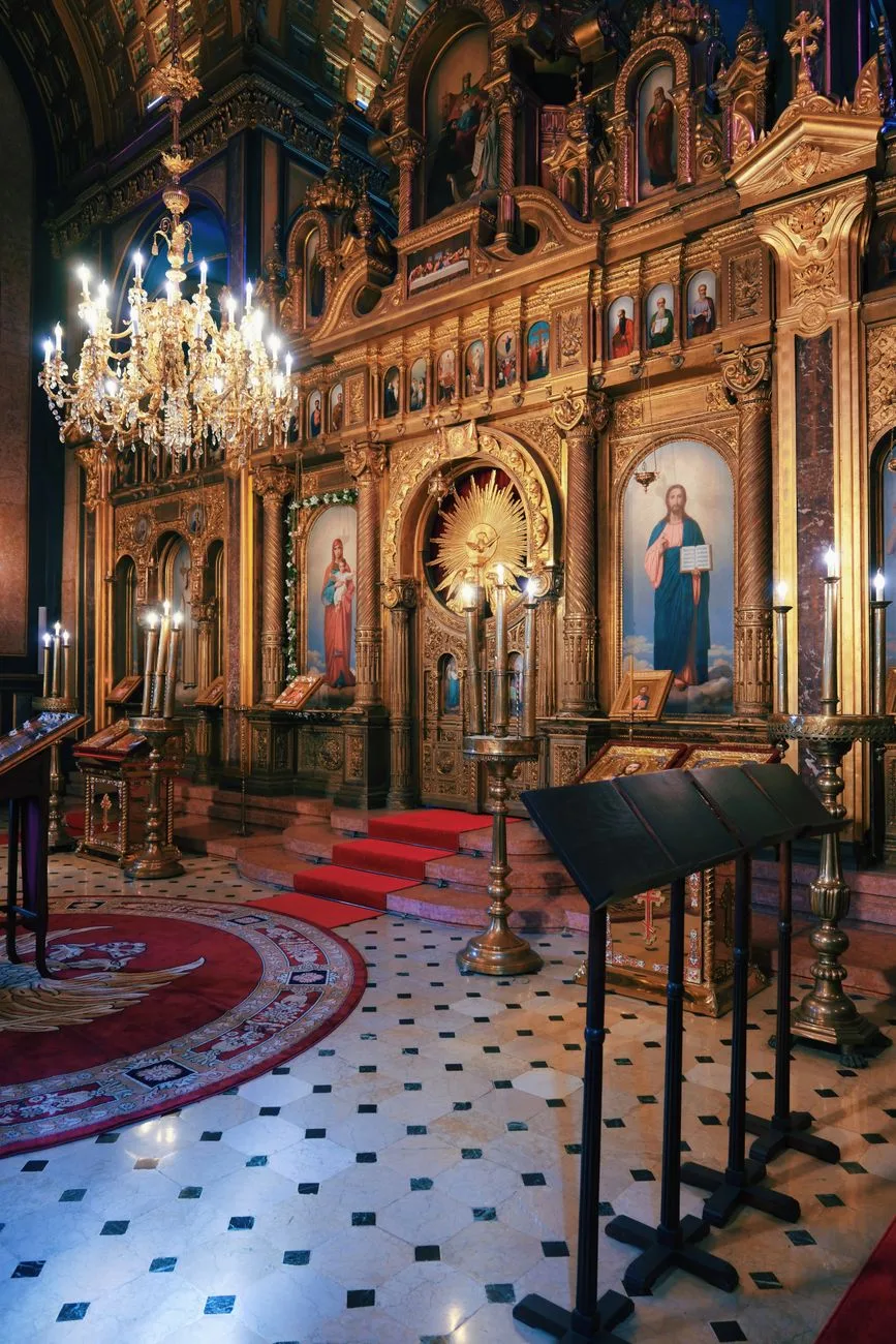 An ornate Orthodox church interior with golden icons and chandeliers.