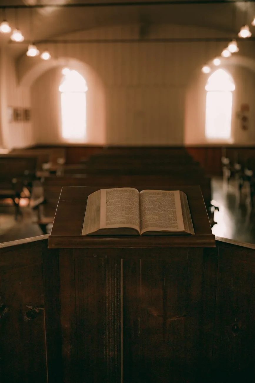 An open Bible on a wooden podium in a warm, vintage-style church interior.
