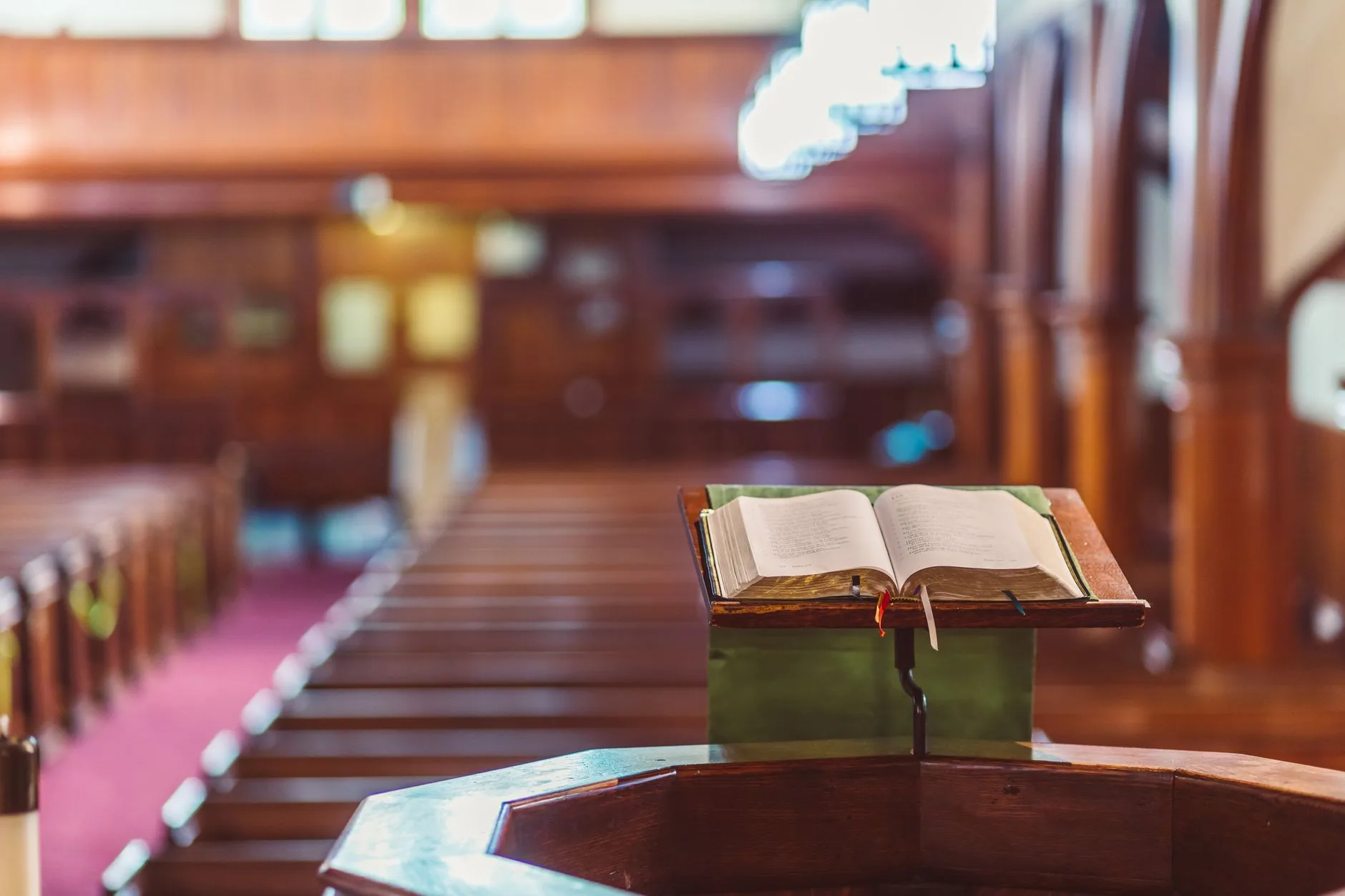An open Bible on a wooden pulpit with blurred pews in the background.