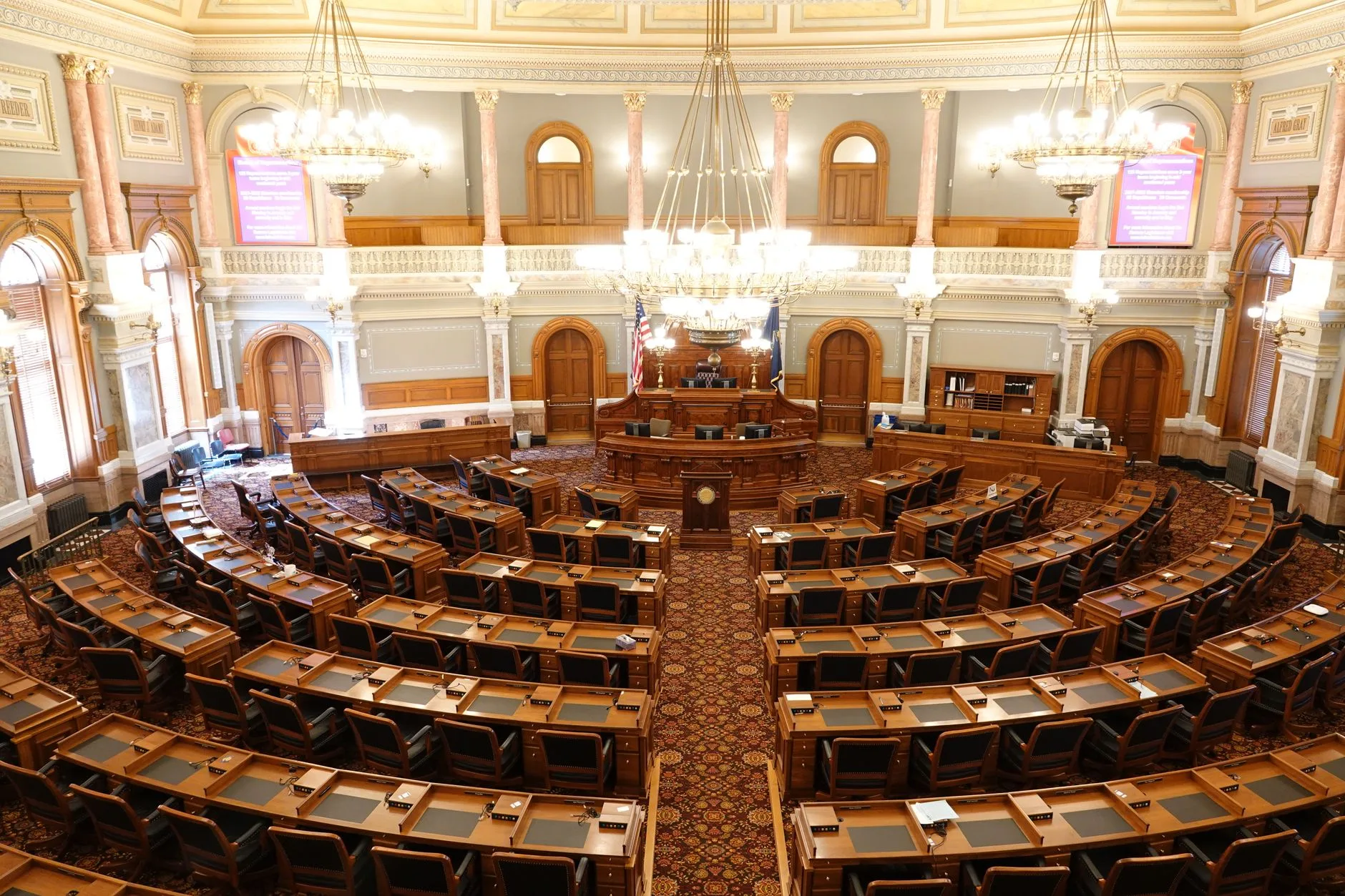 A wide view of an ornate legislative chamber with empty seats and chandeliers.