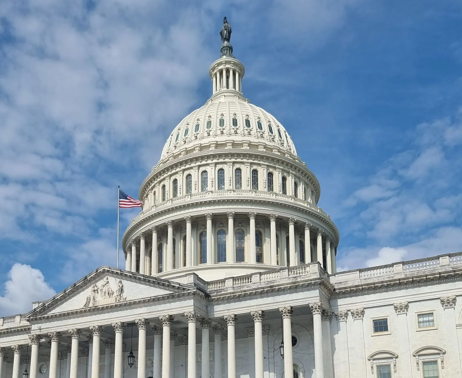 A striking view of the US Capitol dome with a flag against a blue sky.