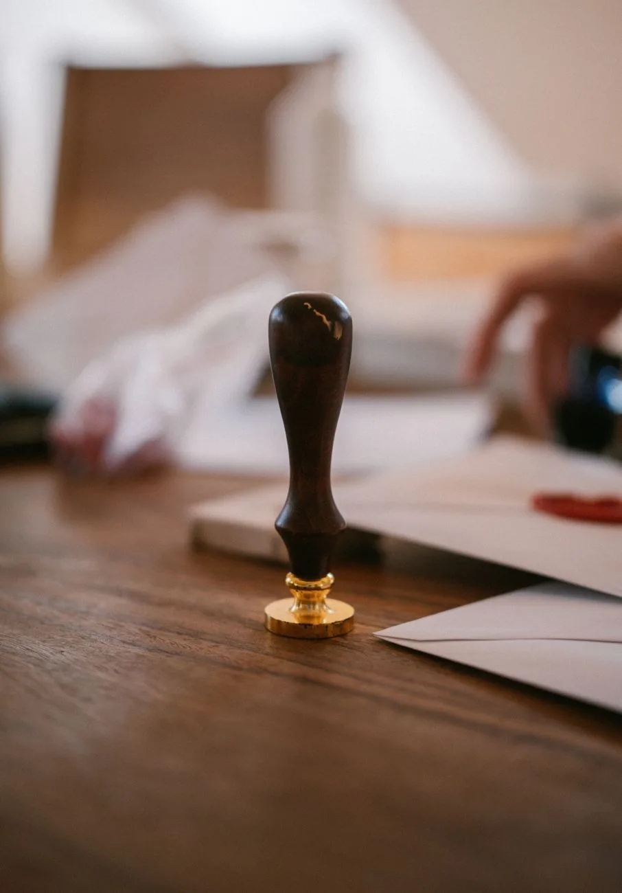 A vintage wax seal stamp resting on a wooden desk beside envelopes.