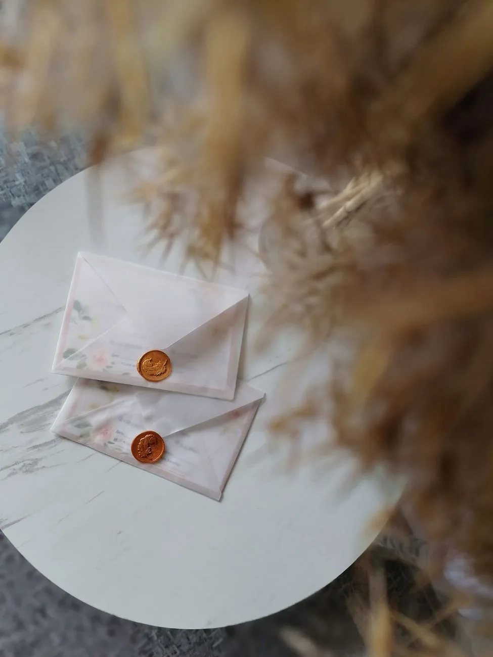 Two floral envelopes sealed with wax on a round marble table.