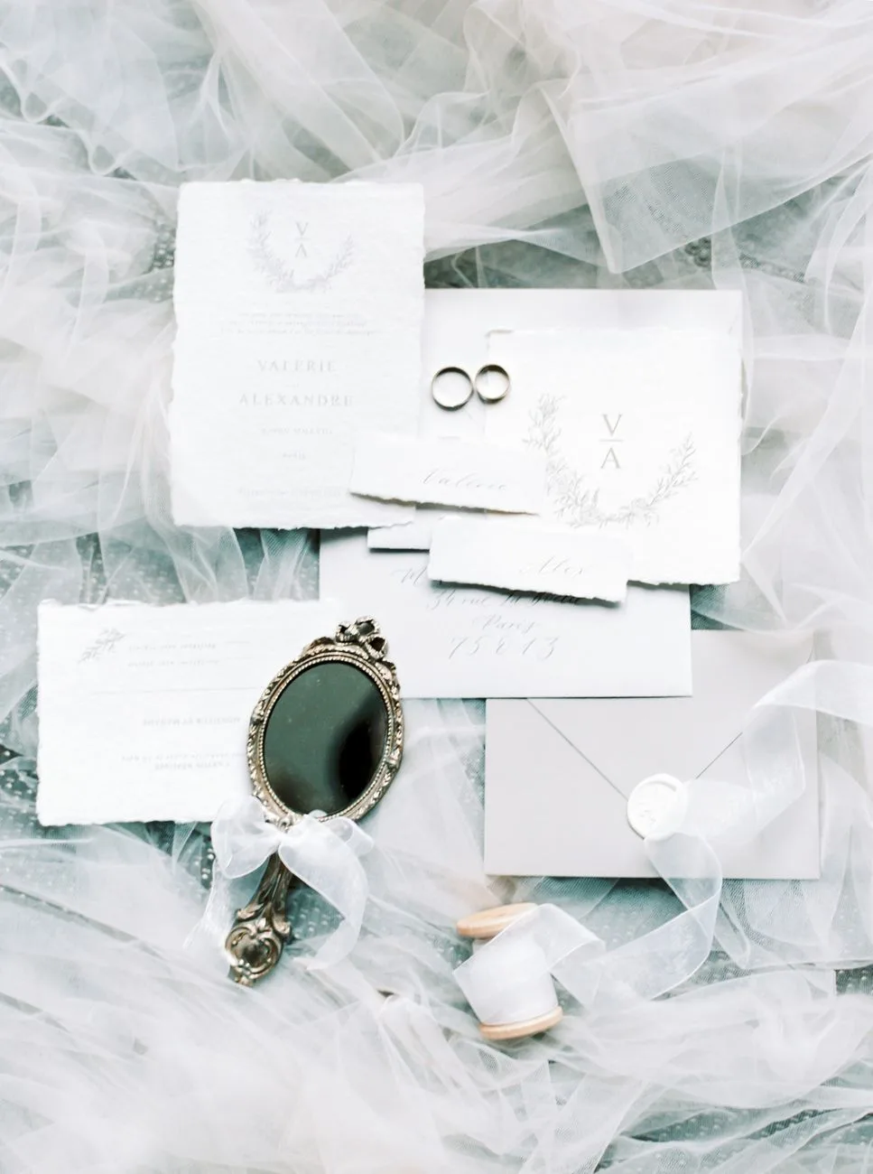 A charming flat lay of wedding invitations, rings, and a vintage mirror.