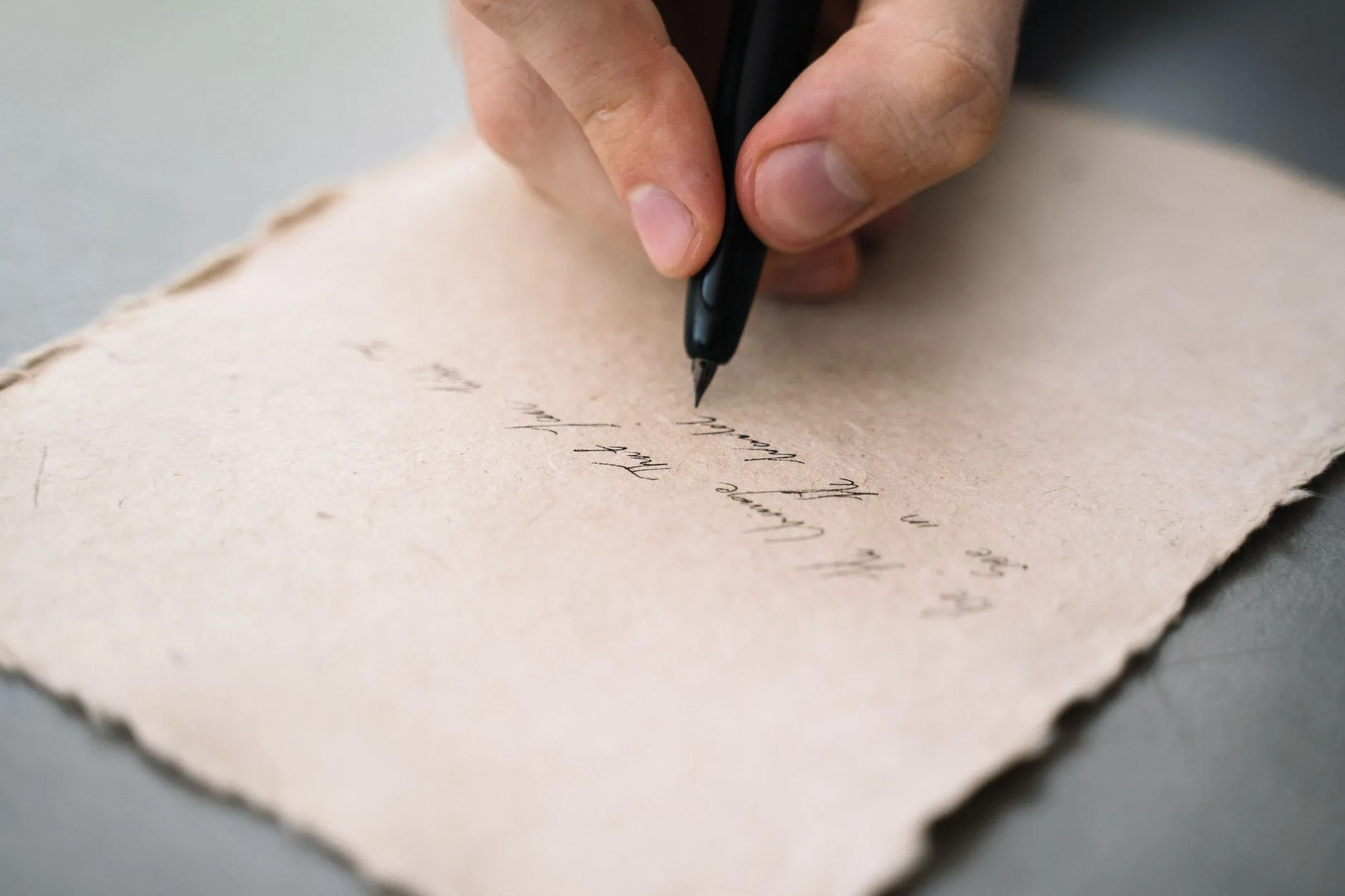 A close-up of a person's hand writing with a pen on textured paper.