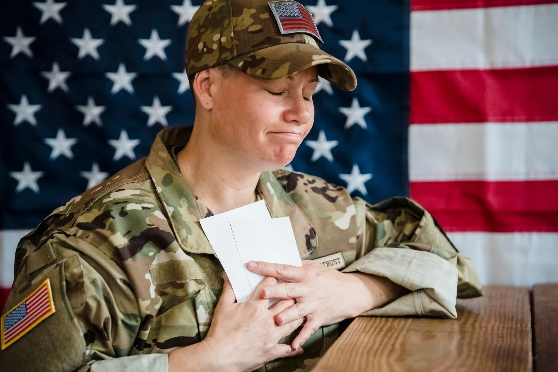 A soldier in uniform holding envelopes in front of an American flag.