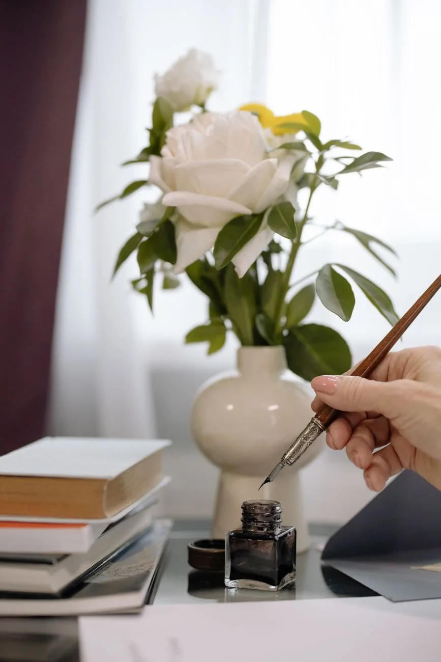 Elegant handwriting with a fountain pen beside a rose vase on a desk.