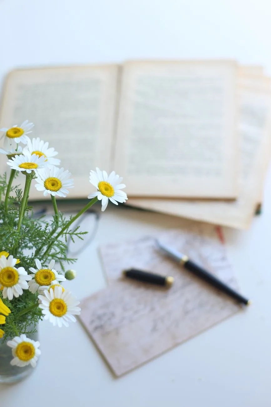 An elegant arrangement of daisies, an open book, and a pen.