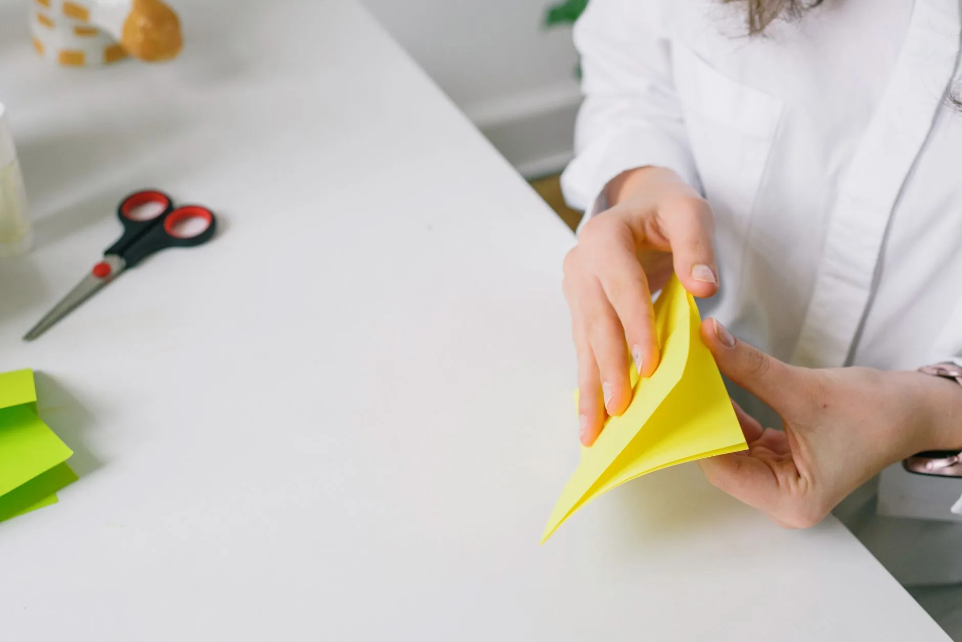 A person carefully folding paper at a well-lit desk.