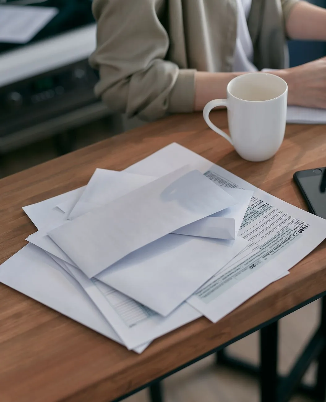 A casual workspace with envelopes, documents, and a coffee cup on a wooden table.