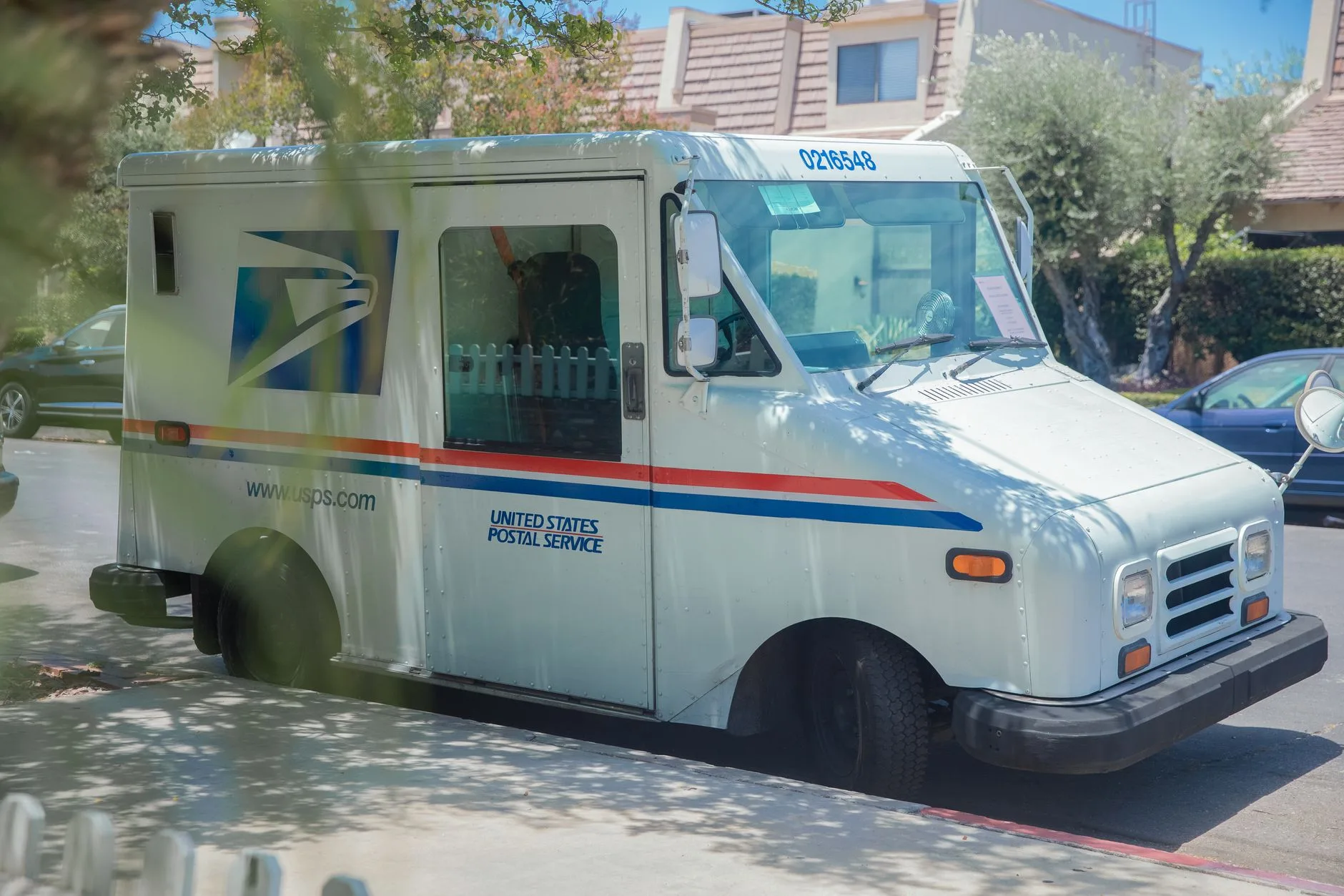 USPS delivery van parked on a sunny residential street.