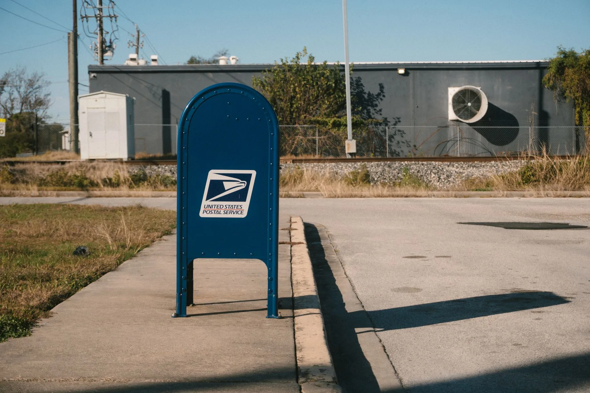 A blue USPS mailbox on a sunny suburban street.