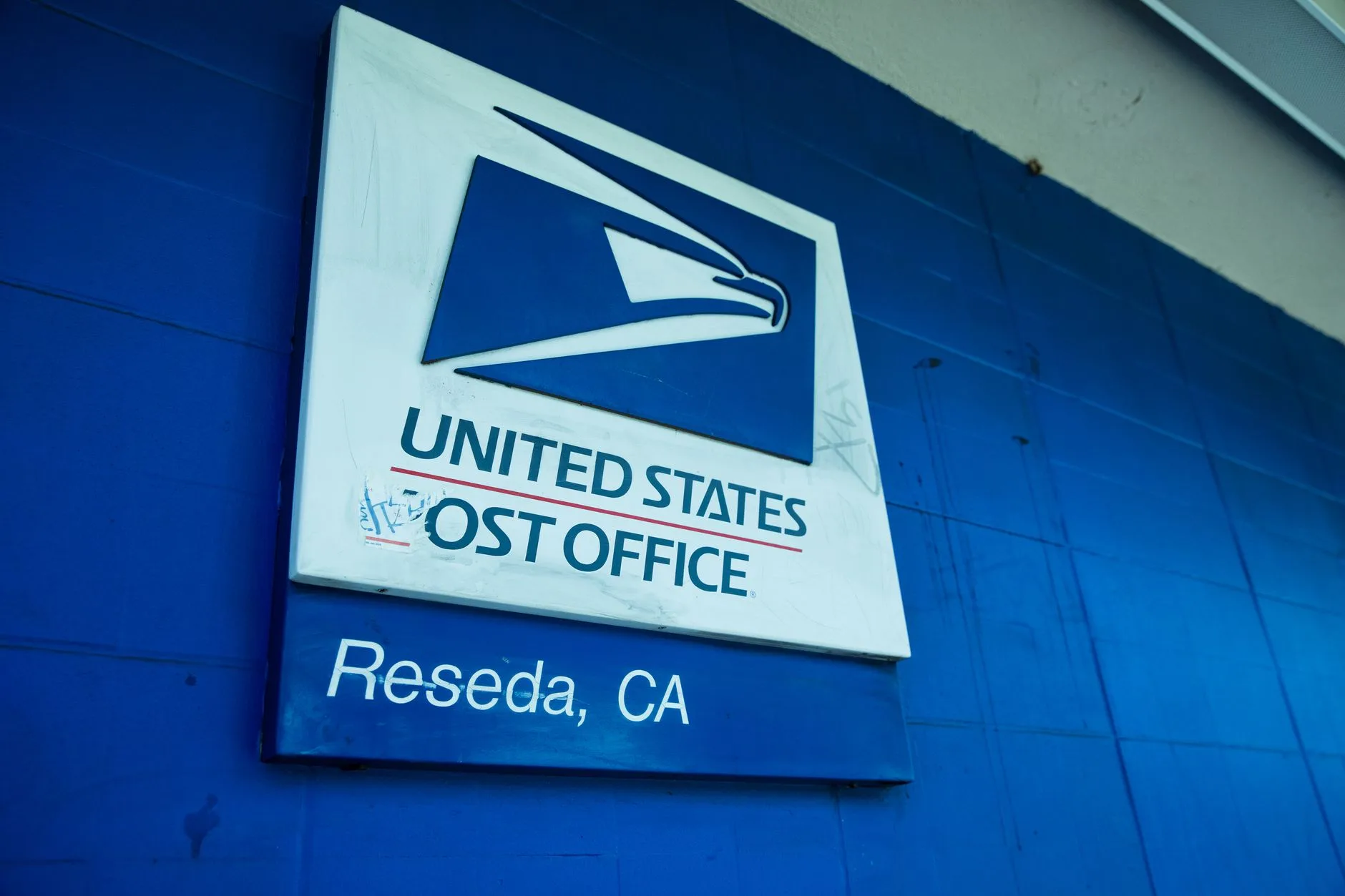 A close-up of the United States Post Office sign against a blue wall.